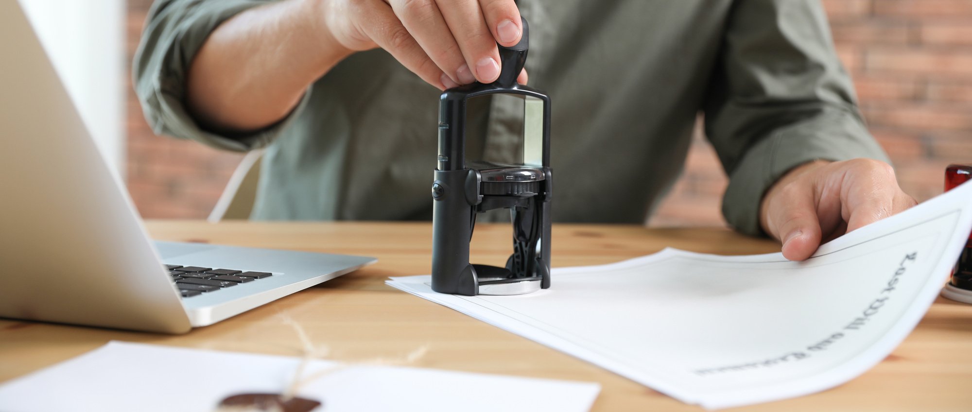 Male Notary Stamping Document at Table in Office, Closeup